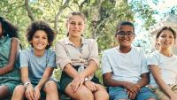 A a group of teenagers sitting on a tree trunk at summer camp.